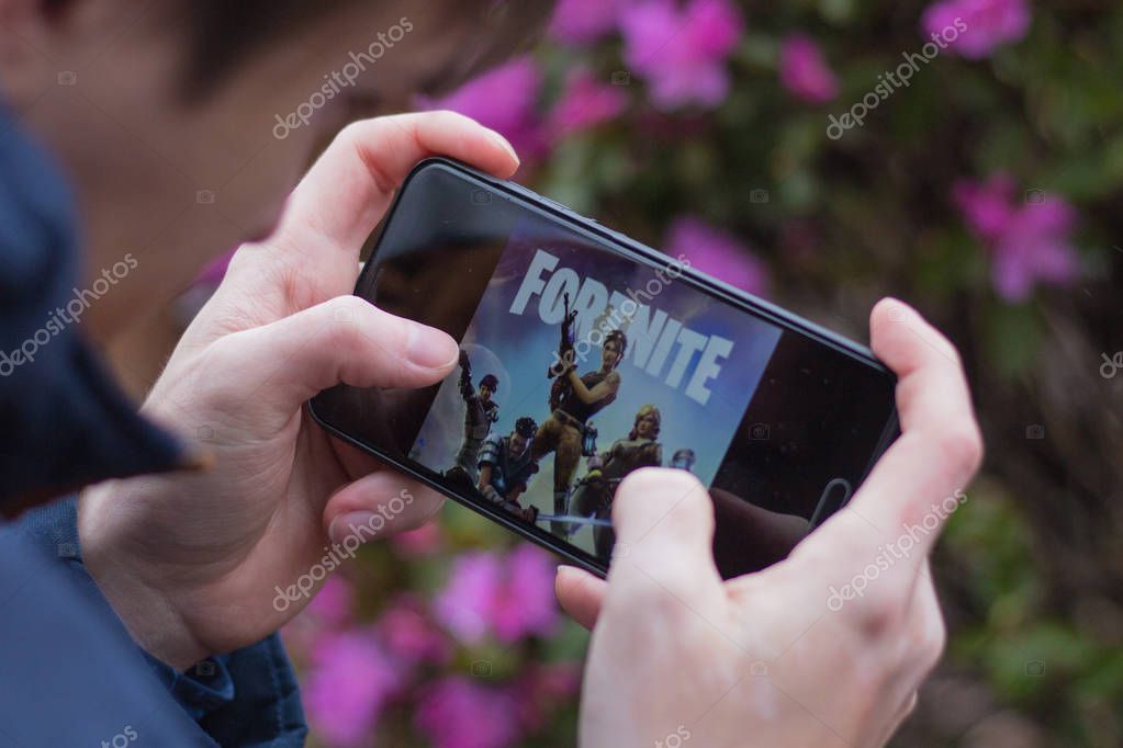 Saint Petersburg, RUSSIA -02 May, 2019: Popular fortnight game on mobile screen. A young guy in the park plays a fortnight.