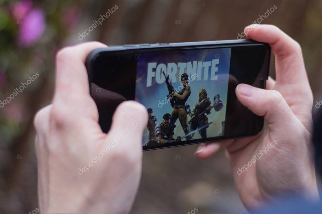 Saint Petersburg, RUSSIA -02 May, 2019: Popular fortnight game on mobile screen. A young guy in the park plays a fortnight.