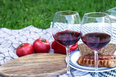 İki bardak elit kırmızı şarap. Arka planda ızgara sosis, sebze, ekmek vardır.