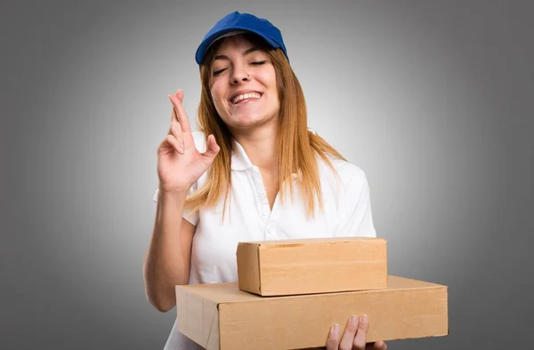 Delivery woman with her fingers crossing on grey background