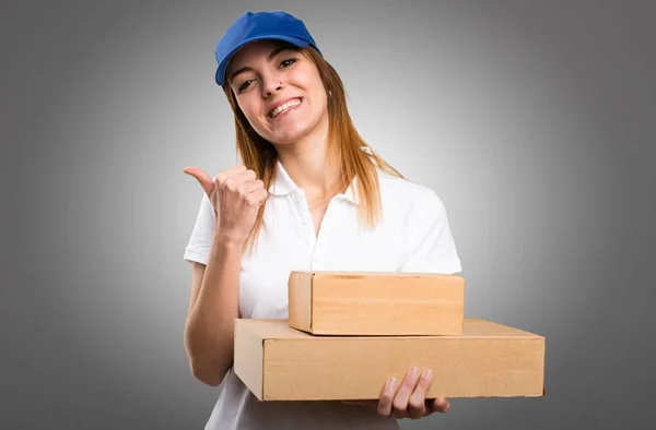 Delivery woman with thumb up on grey background