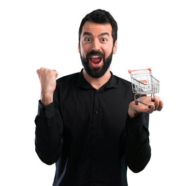 Beyaz arka plan üzerinde tutmak bir süpermarket arabası oyuncak sakallı yakışıklı adam