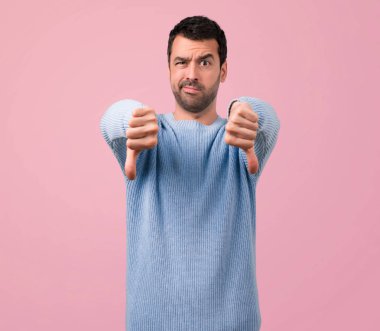 Yakışıklı adam, pembe arka plan başparmak aşağı negatif ifade işaretiyle gösterilen