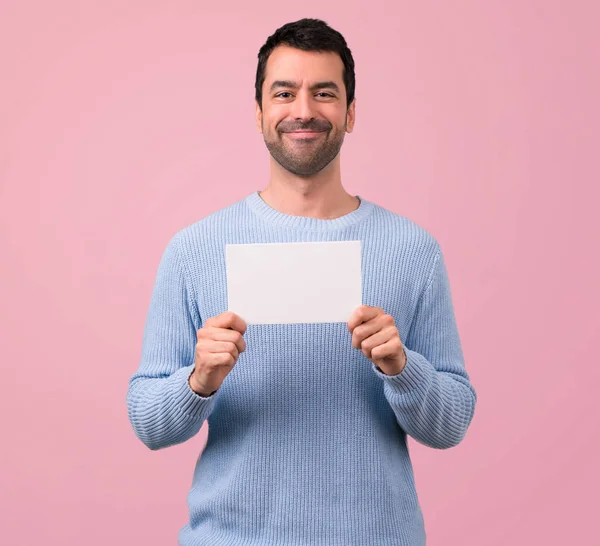 穿着蓝色毛衣的男子在粉红色背景上插入一个概念的空白白色标语牌 — 图库照片