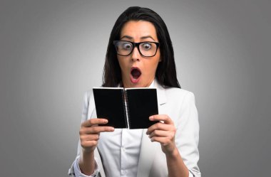 Gri arka plan üzerine bir not defteri tutan gözlük güzel kadın