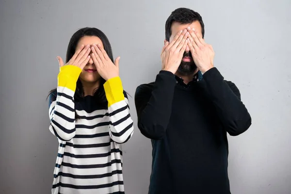 Couple covering their eyes on grey background