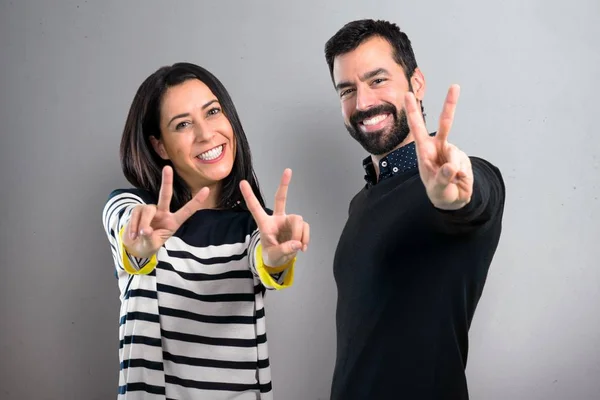 Couple making victory gesture on grey background