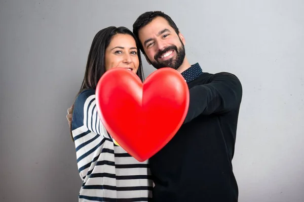 Couple holding a heart toy on grey background