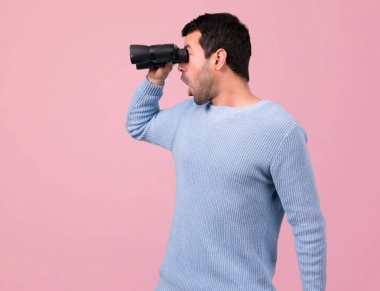 Pembe bir arka plan üzerinde siyah dürbün ile mavi kazaklı adam