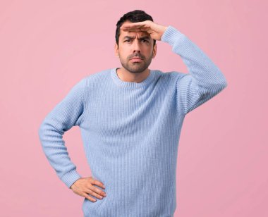 Mavi kazak uzakta el ile seyir ile bir şey, pembe arka plan bakmak için adam