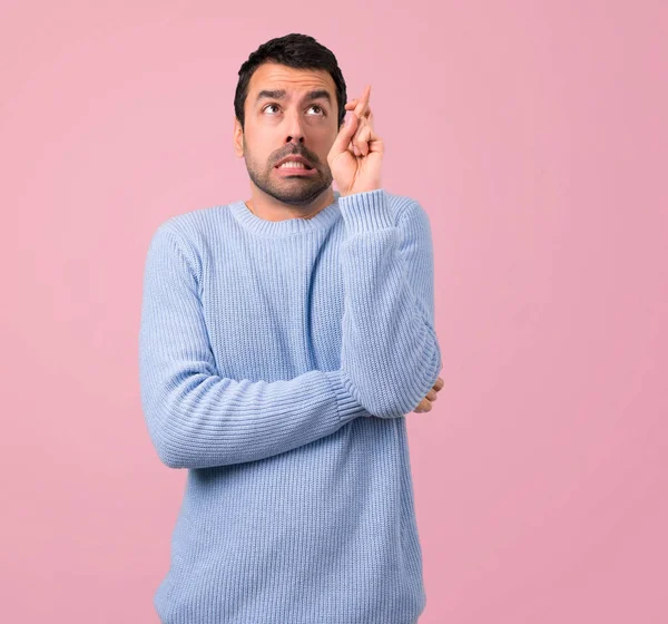 En iyi dilek ve geçiş parmak ile mavi kazaklı adam. Bir dilek yapma. pembe arka plan