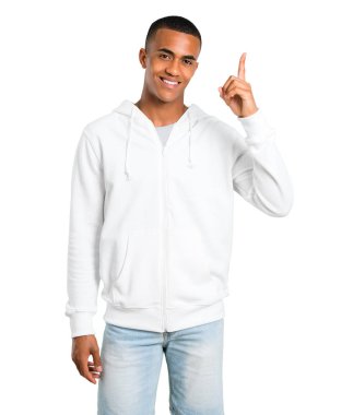Esmer genç adam ile gösterilen ve işareti en iyi izole beyaz zemin üzerinde bir parmak kaldırma beyaz sweatshirt