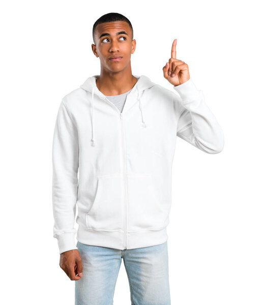 Dark-skinned young man with white sweatshirt standing and thinking an idea pointing the finger up on isolated white background