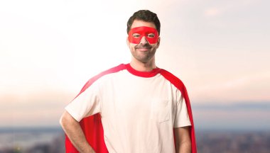 Silah, kalça ile poz ve gün batımı bir arka plan üzerinde gülümseyen maskesi ve kırmızı pelerin adamla süper kahraman