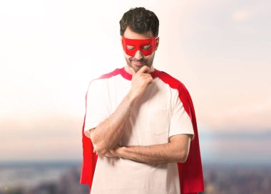 Süper kahraman adam ayakta ve çene günbatımı bir arka plan üzerinde el ile bakıyordu maskesi ve kırmızı pelerin ile