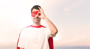 Süper kahraman maske ve kırmızı pelerin adamla komik ve çılgın yüz duygu günbatımı bir arka plan üzerinde yapar.
