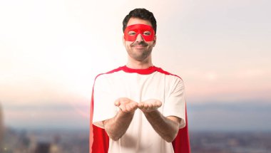 Gün batımı bir arka plan üzerinde bir reklam eklemek için maske ve kırmızı pelerin boşaltmak hayali avuç içinde tutan adamla süper kahraman