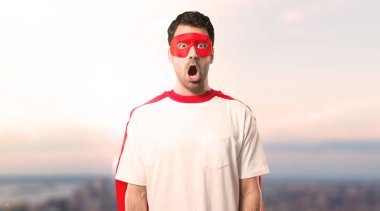Süper kahraman maske ve kırmızı pelerin sürpriz ve şok yüz ifadesi ile olan adam. Çünkü ağzı açık sadece sürpriz bir hediye günbatımı bir arka plan ile