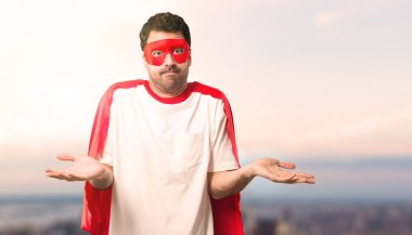 Süper kahraman maske ve önemsiz hale kırmızı pelerin ve şüpheler adamla jest sırasında kaldırma günbatımı bir arka plan üzerinde omuz ve ellerde