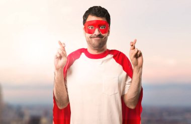 Süper kahraman maske ve kırmızı pelerin ile en iyi dilek ve geçiş parmak adamla. Bir dilek yapma. gün batımı bir arka plan üzerinde