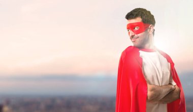 Süper kahraman maske ve kırmızı pelerin günbatımı bir arka plan bir gülümseme ile omuz üzerinden ararken lateral pozisyonda adamla