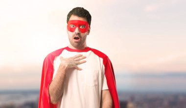 Süper kahraman şaşırttı ve doğru bakarken şok maskesi ve kırmızı pelerin adamla. Gün batımı bir arka plan üzerinde etkileyici yüz duygu