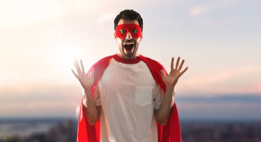 Maskesi ve kırmızı pelerin yapım sürpriz bir jest günbatımı bir arka plan üzerinde olan süper kahraman adam