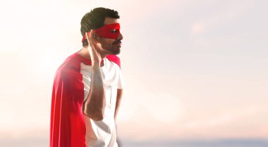 Süper kahraman maske ve kırmızı pelerin günbatımı bir arka plan üzerine bir şey dinlerken adamla