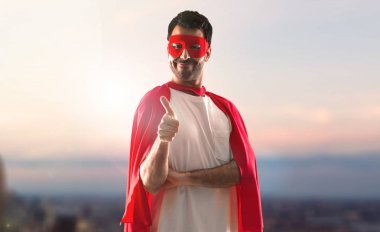 Süper kahraman maske ve kırmızı pelerin günbatımı bir arka plan üzerinde başparmak ile adamla