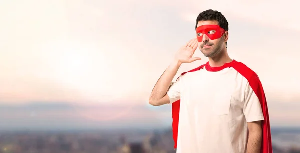 スーパー ヒーロー マスクと赤マントは 夕日を背景に耳に手を置くことによって何かを聞く男 — ストック写真
