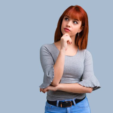 Ayakta ve mavi arka plan üzerinde bir fikir düşünme genç Kızıl saçlı kız