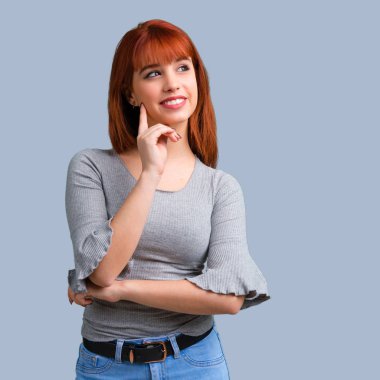 Ayakta ve mavi arka plan üzerinde bir fikir düşünme genç Kızıl saçlı kız