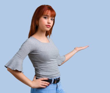 Geri mavi zemin üzerine işaret parmağı ile işaret eden genç Kızıl saçlı kız