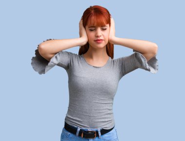 Her iki kulak mavi arka plan üzerinde elleriyle kapsayan genç Kızıl saçlı kız