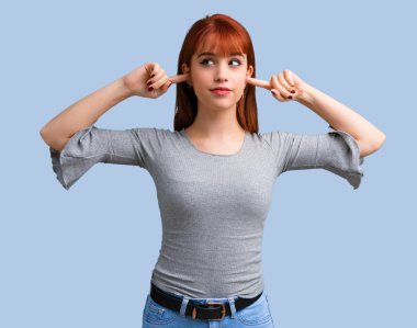 Her iki kulak mavi arka plan üzerinde elleriyle kapsayan genç Kızıl saçlı kız