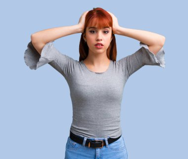 Genç Kızıl saçlı kız mutsuz ve bir şey ile sinirli. Mavi arka plan üzerinde negatif yüz ifadesi