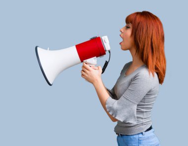 Mavi arka plan üzerinde bir megafon ile bağırarak genç Kızıl saçlı kız