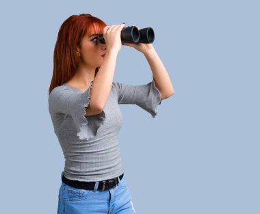 Mavi arka plan üzerinde siyah dürbün ile genç Kızıl saçlı kız