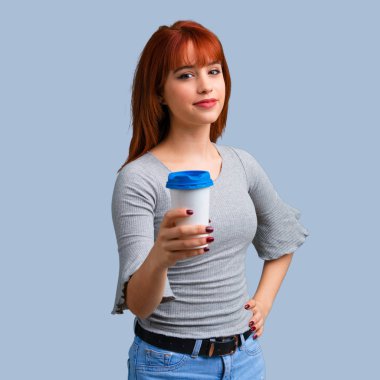 Sıcak kahve paket servisi olan restoran kağıt bardak mavi arka plan üzerinde tutan genç Kızıl saçlı kız