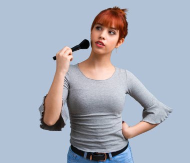 Makyaj fırça üzerinde mavi arka plan ile genç Kızıl saçlı kız