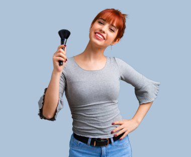 Makyaj fırça üzerinde mavi arka plan ile genç Kızıl saçlı kız