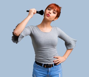 Makyaj fırça üzerinde mavi arka plan ile genç Kızıl saçlı kız