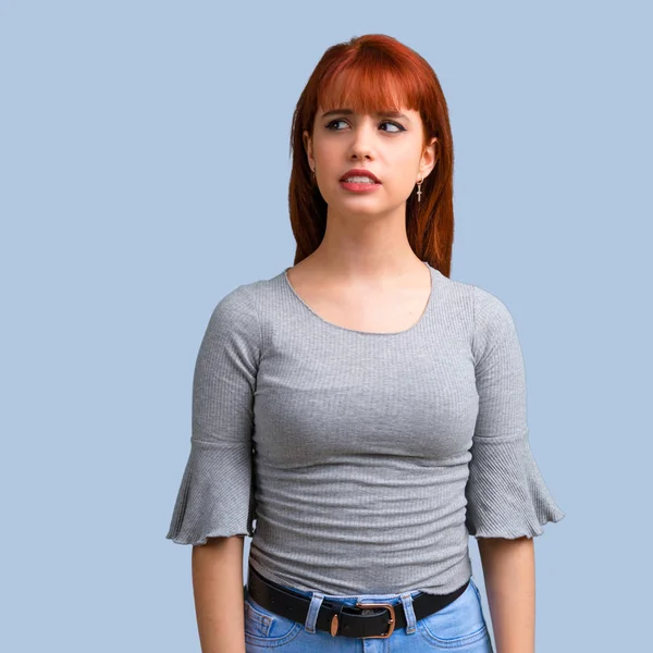 Biraz gergin ve korkmuş mavi zemin üzerine genç Kızıl saçlı kız