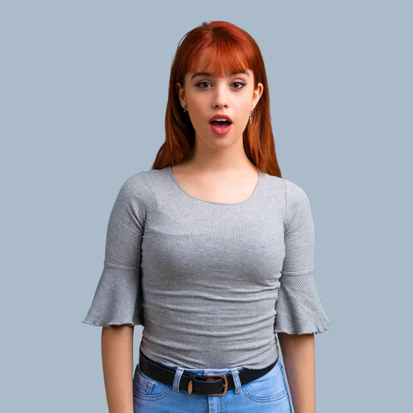 Sürpriz ve mavi zemin üzerine şok yüz ifadesi ile genç Kızıl saçlı kız