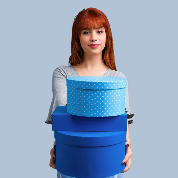 年轻的红头发女孩手持礼品盒在蓝色的背景手 — 图库照片