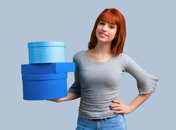 年轻的红头发女孩手持礼品盒在蓝色的背景手 — 图库照片