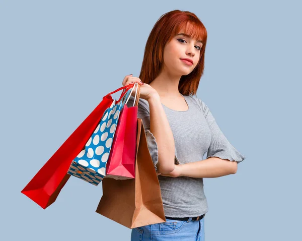 青の背景にたくさんの買い物袋を保持している若い赤毛の女の子 — ストック写真