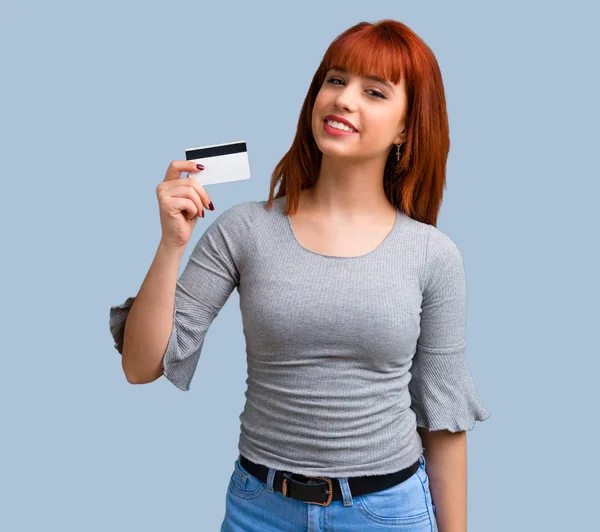Mavi arka plan üzerinde bir kredi kartı tutan genç Kızıl saçlı kız