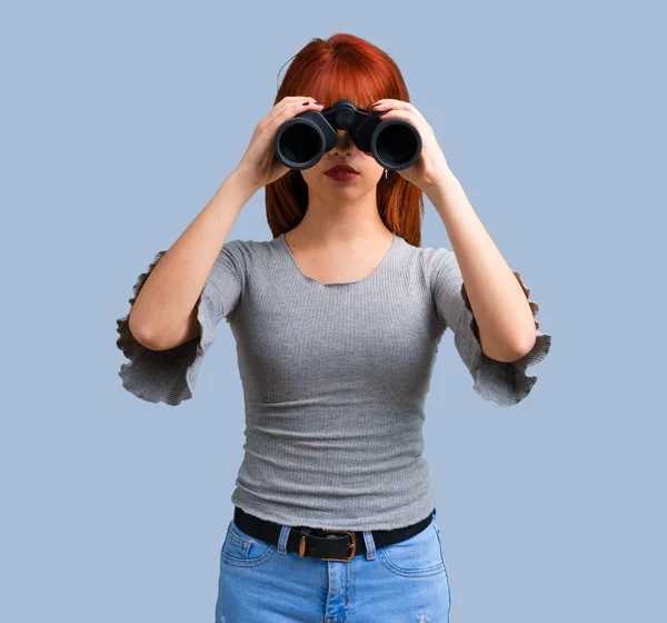 青の背景に黒の双眼鏡と若い赤毛の女の子 — ストック写真