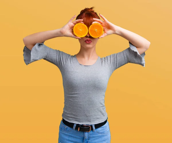 オレンジ色の背景にガラスとオレンジ スライスを着ている若い赤毛の女の子 — ストック写真
